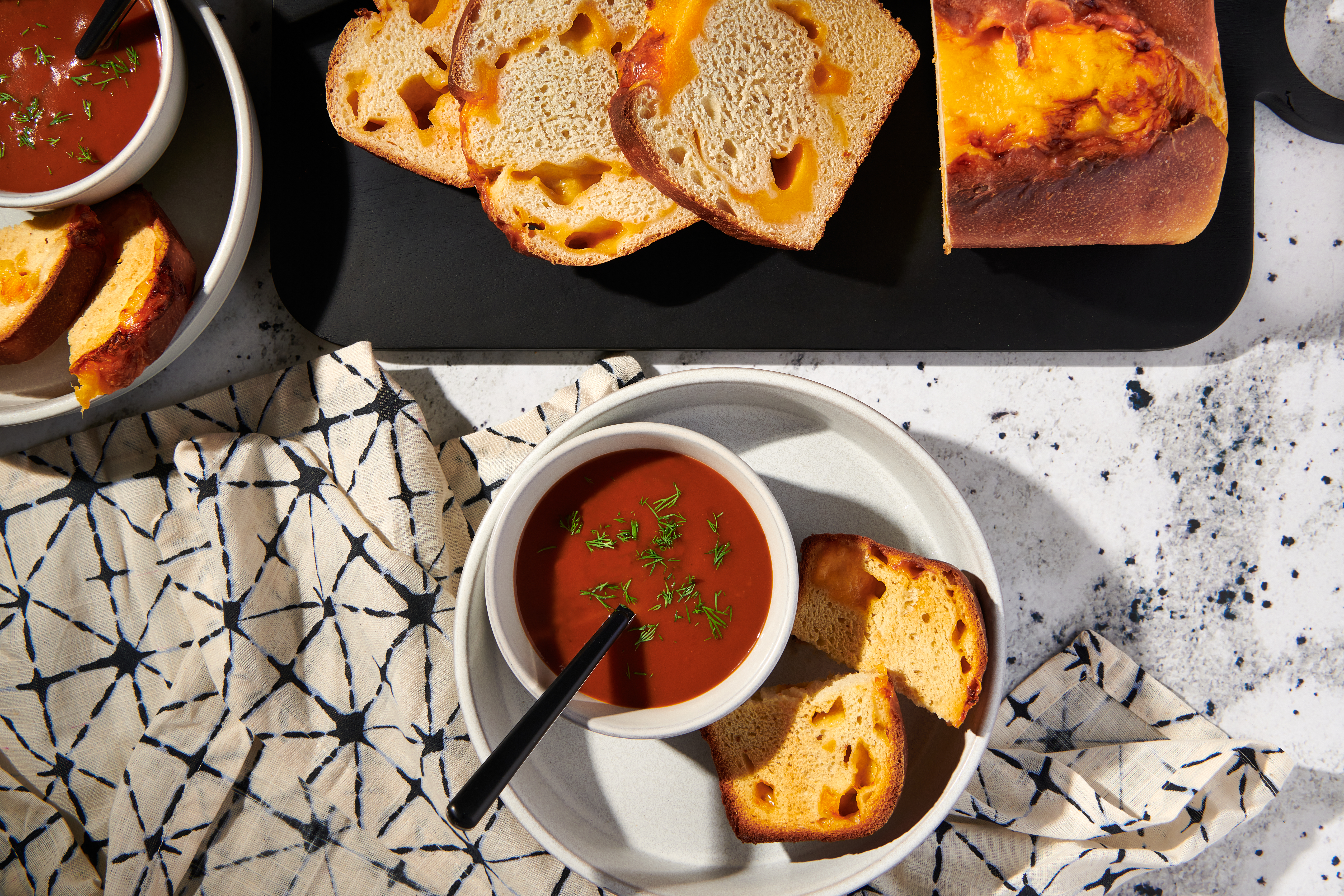 A sliced loaf of cheese bread arranged on a table with a bowl of tomato soup.
