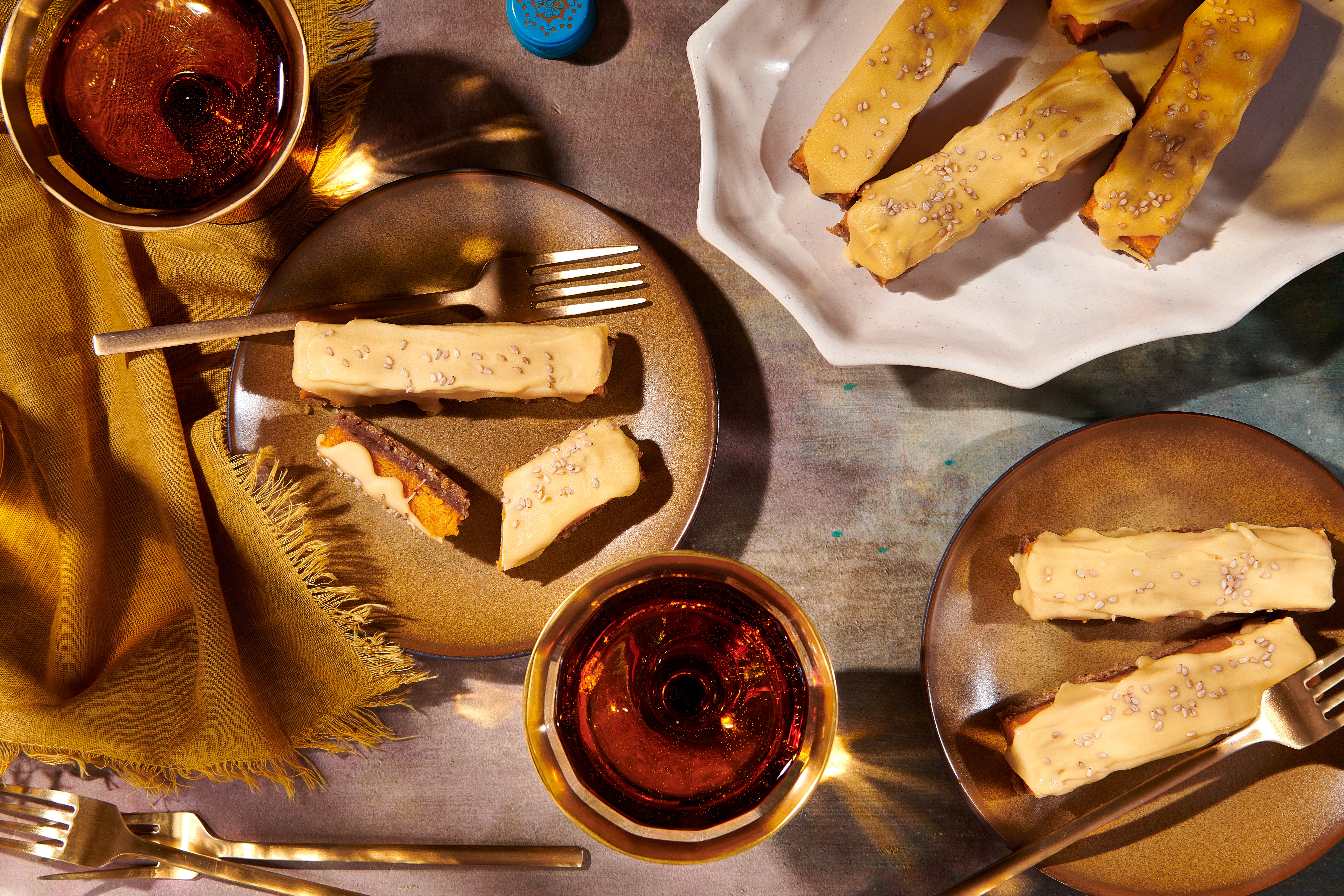 An assortment of sweet potato cheesecake bars arranged on small plates, with glasses of red wine next to them.
