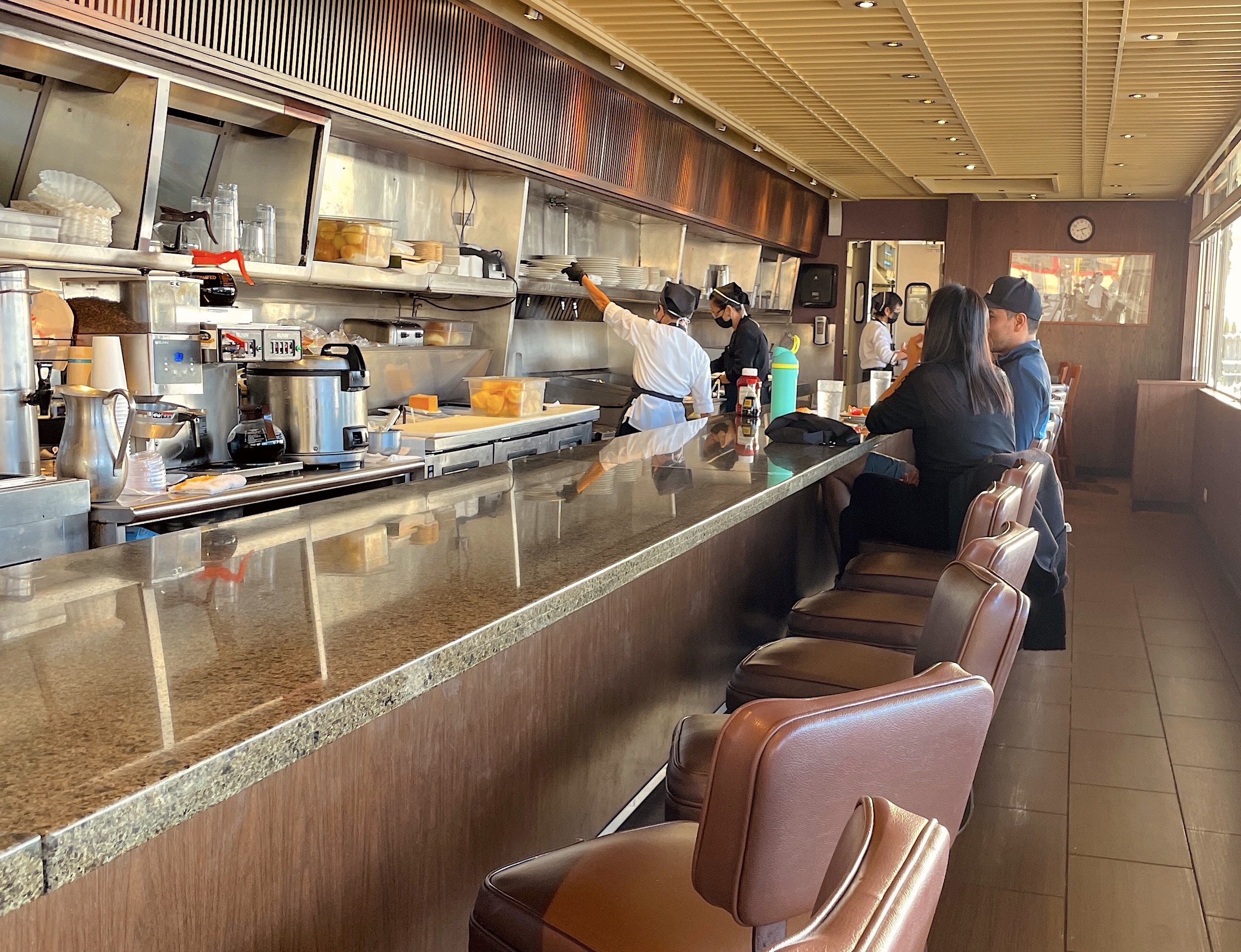 Customers sit on stools at a thin counter inside a diner.
