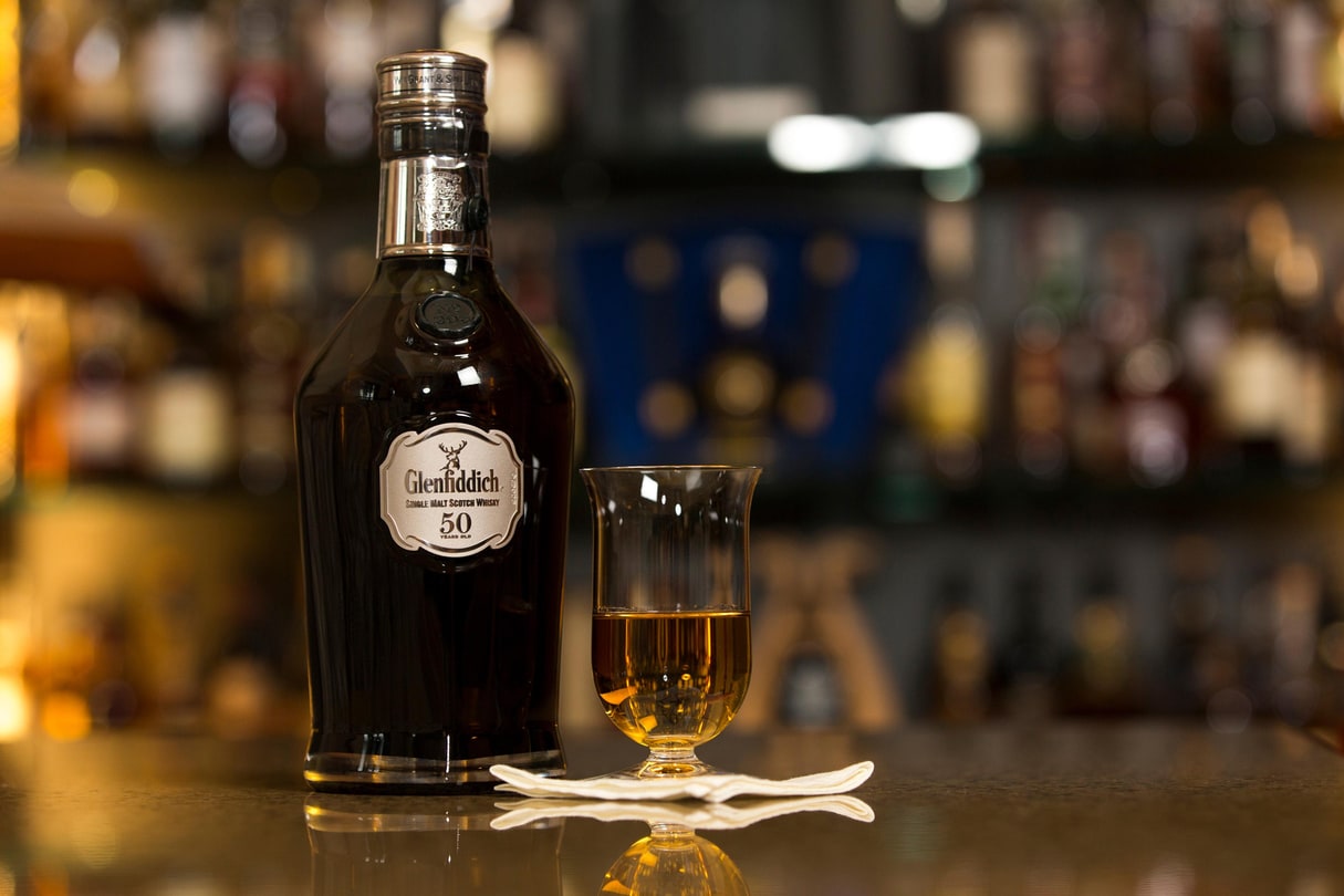A bottle of Glenfiddich next to a snifter glass of Scotch.