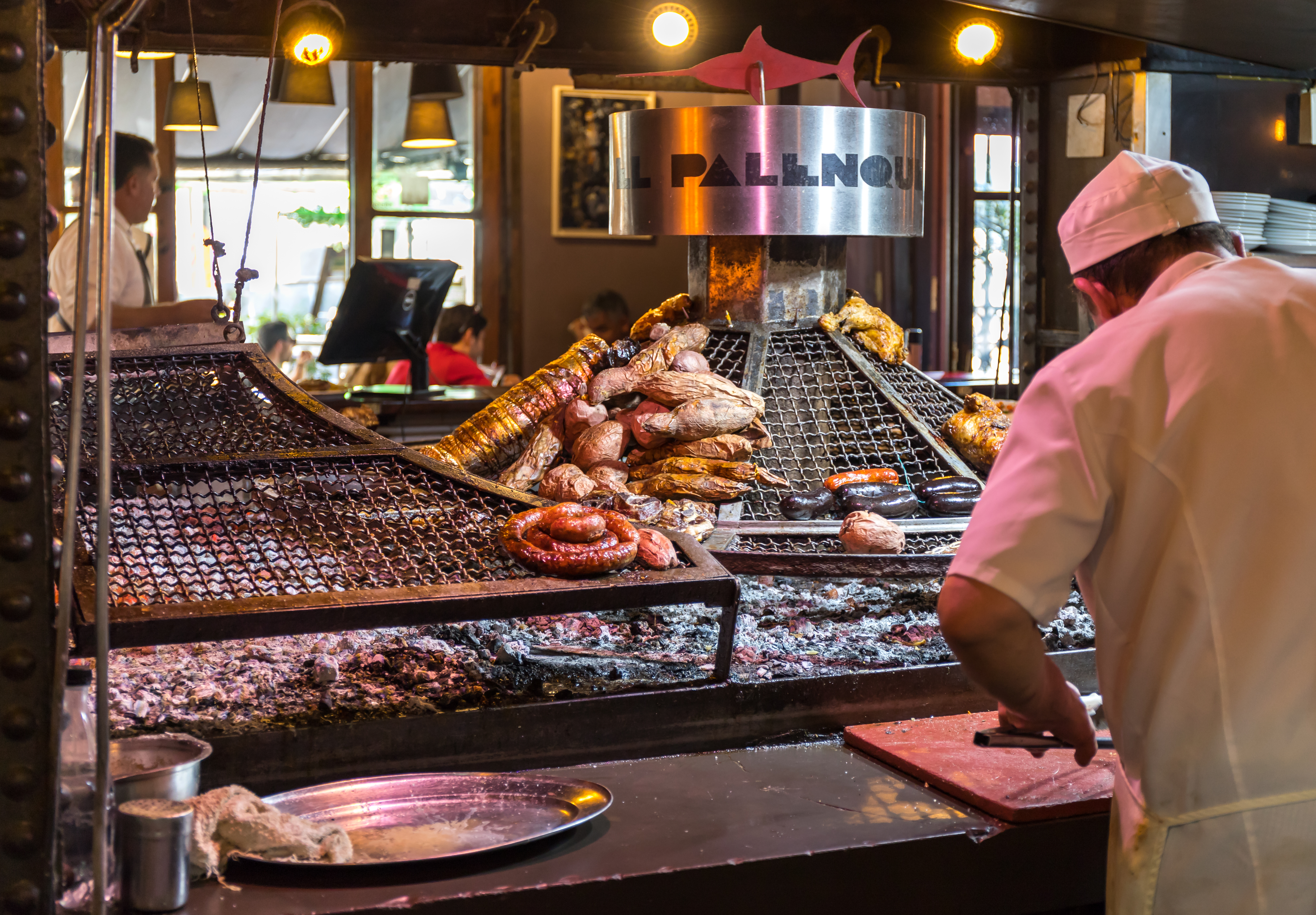 A chef works nearby a grill where meats cook.