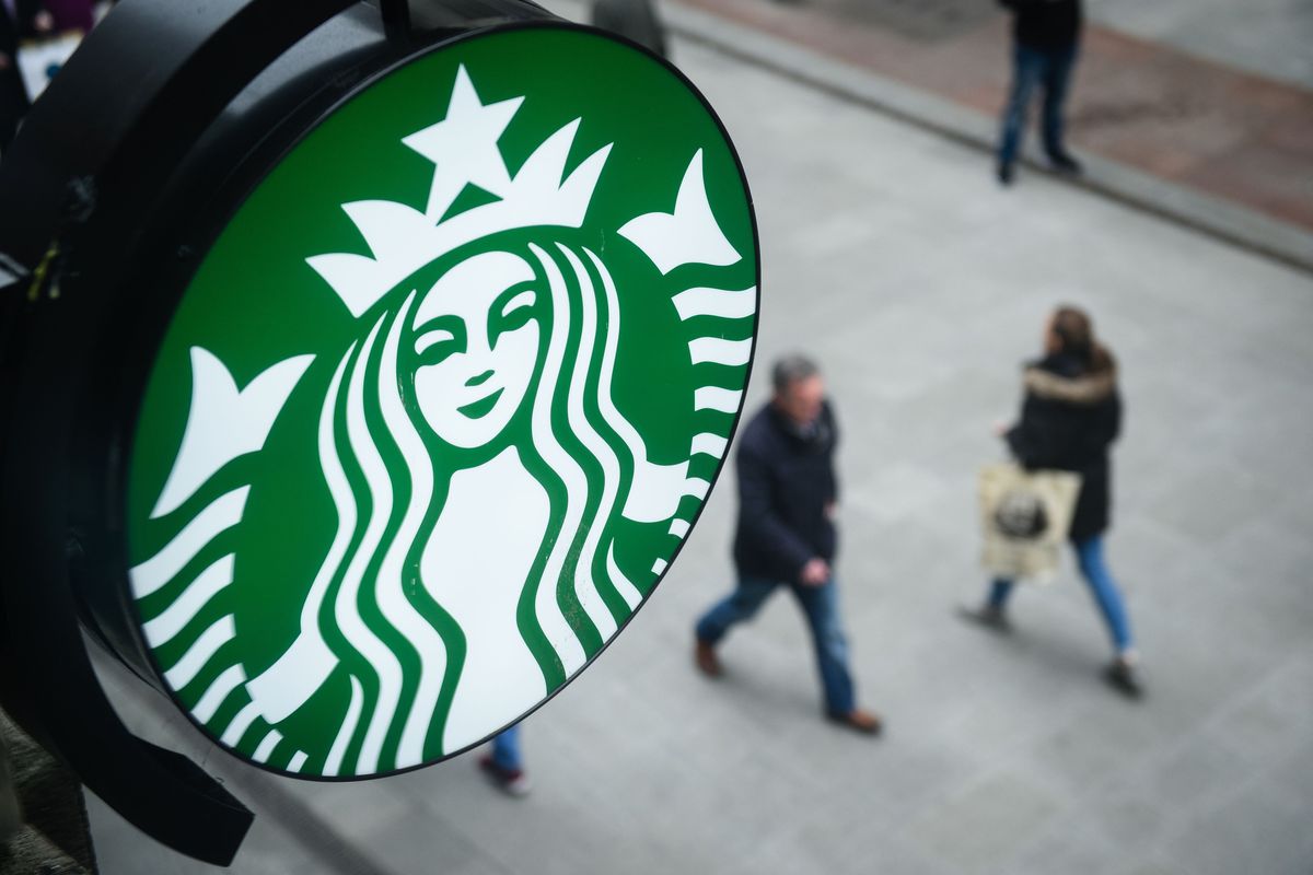 A Starbucks sign looks down on two pedestrians.